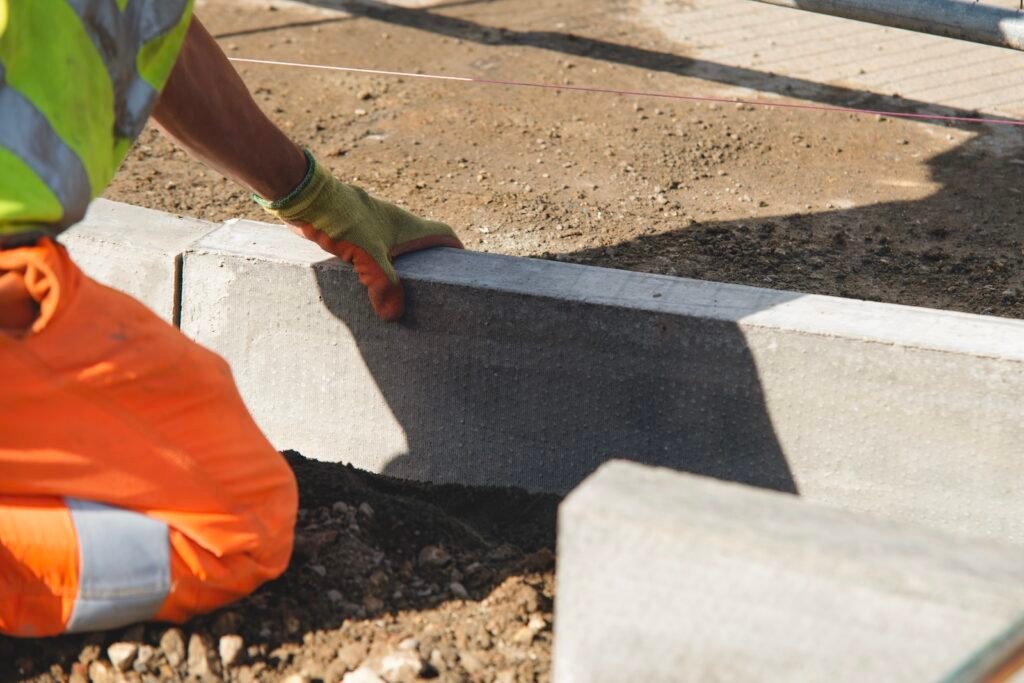 Worker installing concrete kerb for new road construction using rubber mallet