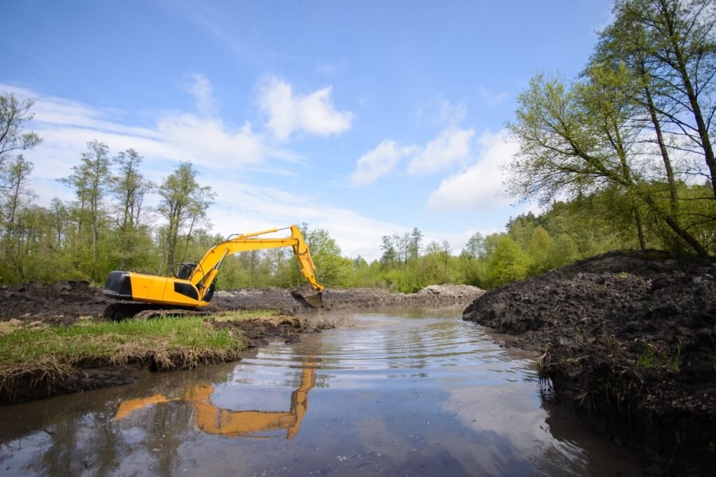 Excavator near the lake in countryside. Cleaning and making river more deep